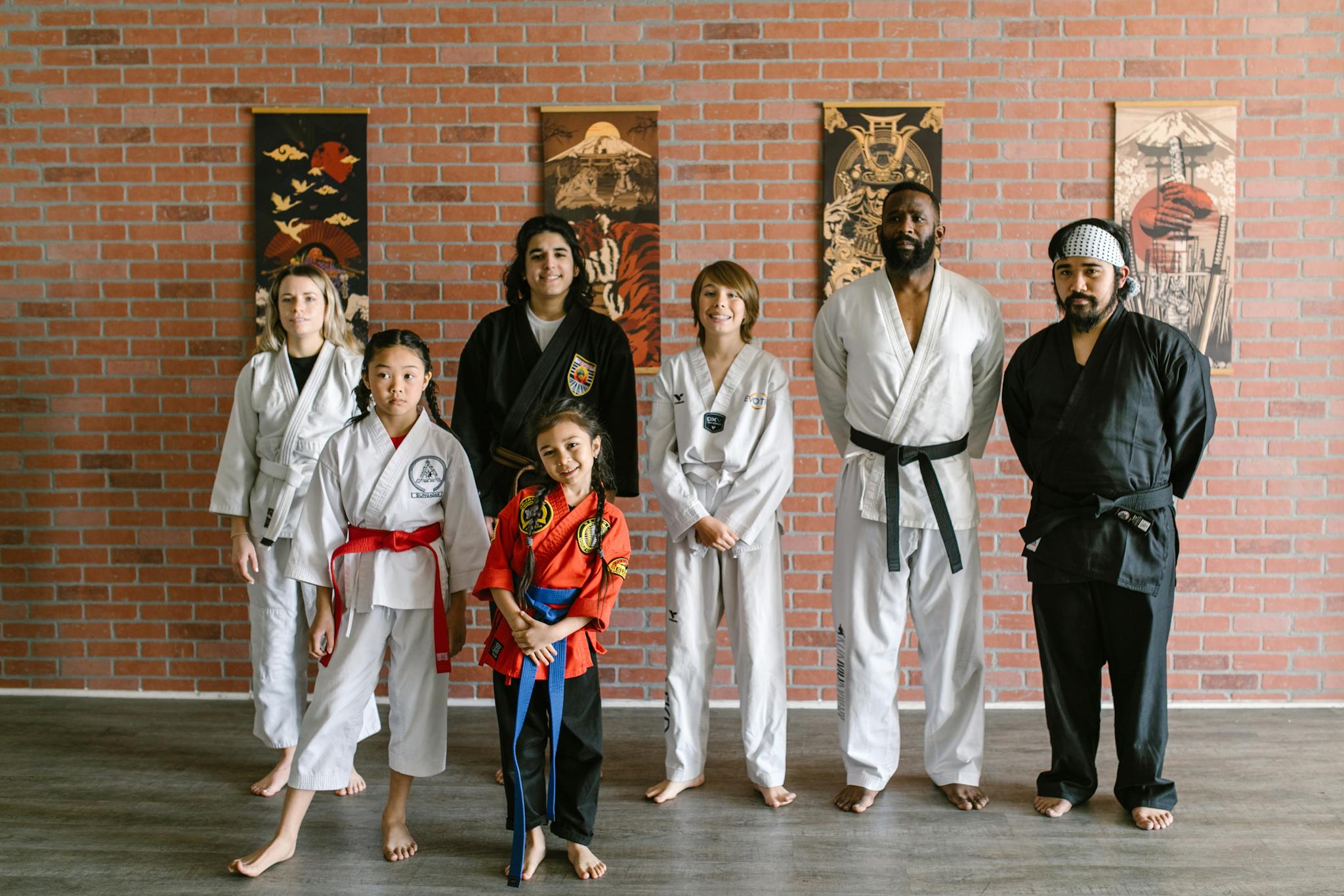 Group of martial artists posing in dojo against brick wall, showcasing diversity.